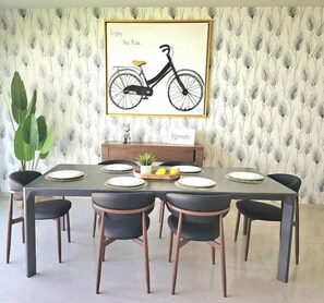 Un comedor con una mesa preparada para seis, sillas, una obra de arte enmarcada de una bicicleta y una planta.