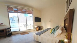 Ein Schlafzimmer mit Bett, Fernseher, Schreibtisch und einem Balkon mit Stuhl.