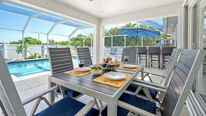 Eine sonnendurchflutete Terrasse mit Pool, Esstisch, Stühlen und Sonnenschirmen.
