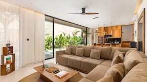 A modern living room with a large sectional sofa, a wooden coffee table, and a view of a pool and greenery outside.