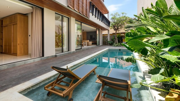 A modern house with a swimming pool, wooden deck, and lush greenery.