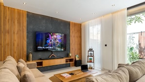 A modern living room with a large flat-screen TV, wooden panel walls, a sofa, a coffee table, and a bookshelf.