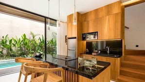A modern kitchen with wooden cabinetry, a black countertop, and a stainless steel stove. There are two wooden bar stools and a glass bowl on the counter.