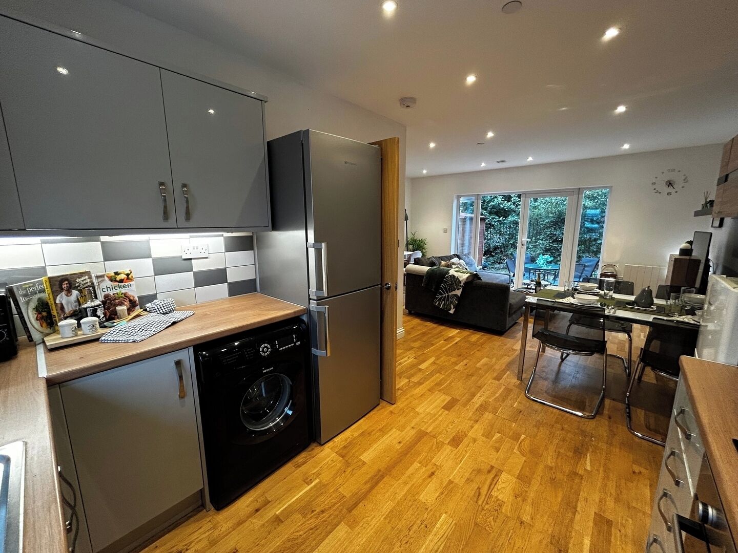 A modern kitchen with grey cabinets, a built-in washing machine, and a dining area with a table and chairs.