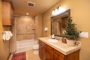 Une salle de bain avec une baignoire, des toilettes, un meuble-lavabo avec un miroir et une plante en pot.