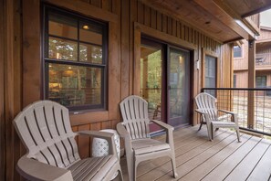 A wooden deck with Adirondack chairs and a glass door leading to an interior space.