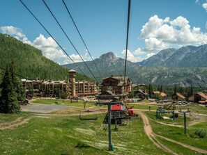 A ski resort with a cable lift system, buildings with multiple floors, and a mountainous backdrop.