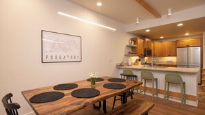 A modern kitchen with wooden cabinets, a stainless steel refrigerator, and a dining area with a wooden table and chairs.