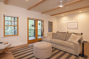 A modern living room with a sofa, ottoman, and a dining table.