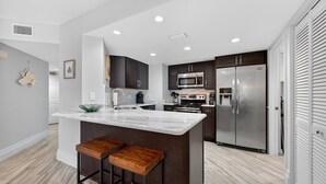 A modern kitchen with dark cabinetry, stainless steel appliances, and a marble island with stools. - New listing! Direct oceanfront 2/2 with private balcony, heated pool, and hot tub (New Smyrna Beach)
