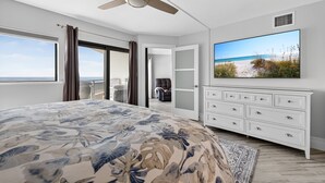 A bedroom with a large bed, a ceiling fan, a TV, and a view of the beach. - New listing! Direct oceanfront 2/2 with private balcony, heated pool, and hot tub (New Smyrna Beach)