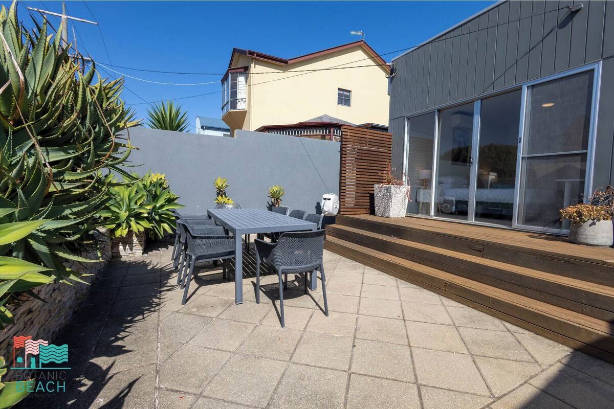 A patio with a table and chairs, surrounded by plants and a grey wall.
