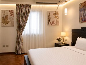 Une chambre d’hôtel avec un lit, une table de chevet avec une lampe, une fenêtre avec des rideaux légers et des œuvres d’art murales.