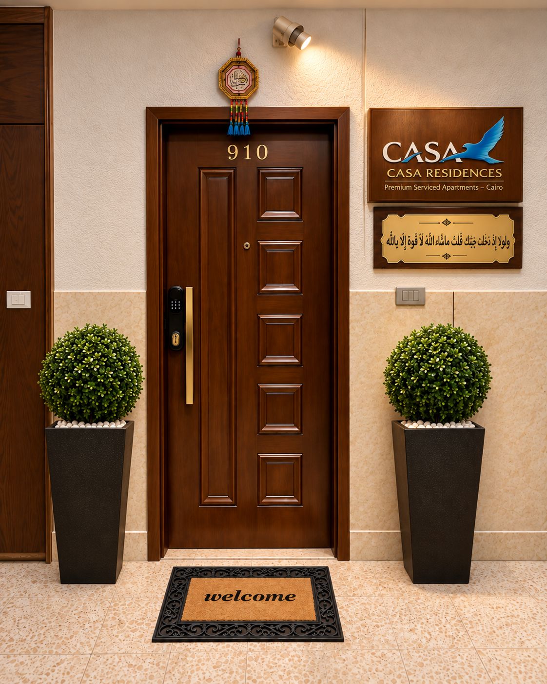 Een hotelentree met een houten deur waarop '910' staat, een welkomstmat, twee potplanten en een bordje met 'CASA CASA RESIDENCES Premium Serviced Apartments - Cairo'.