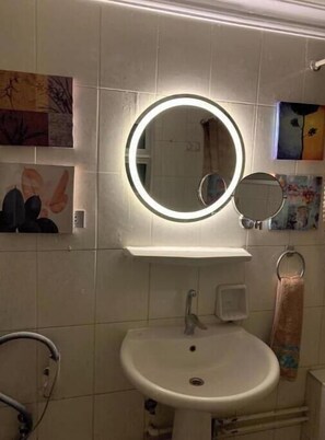 A bathroom with a round mirror with a light, a sink, and a towel rack.