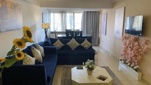 A modern living room with a dark blue sofa, a coffee table, and a TV mounted on the wall. Sunflowers and a vase of flowers are on the coffee table. - Casa De Horyea 2 - الميرغني (Cairo Governorate)