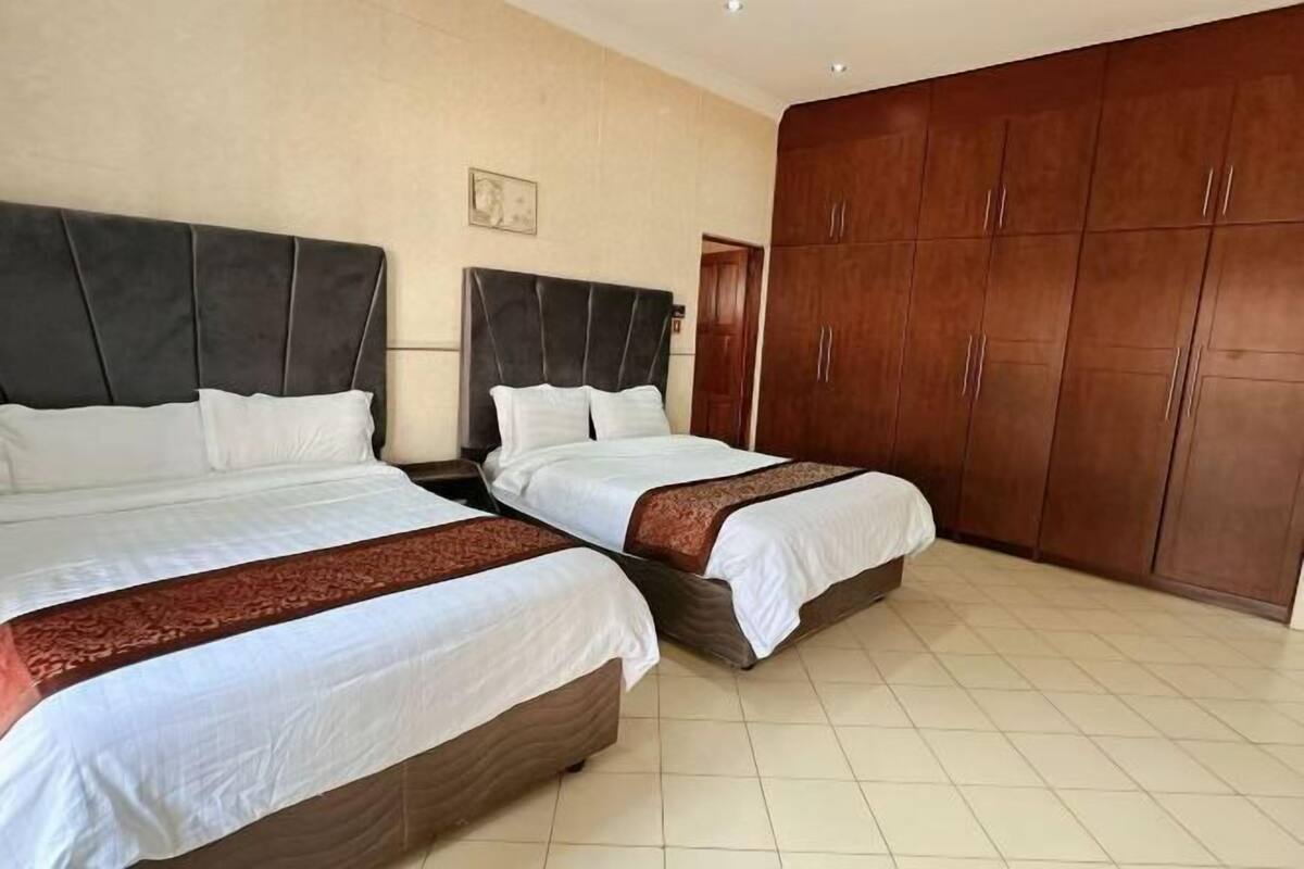A hotel room with two beds, a large wardrobe, and a tiled floor.