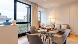 A modern dining area with a glass table, grey chairs, and a sofa in the background. - Stylish Flat with Workspace & Garage by HostWise (Porto)
