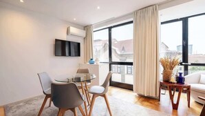 A modern living room with a glass dining table, two chairs, a sofa, and a TV mounted on the wall. - Stylish Flat with Workspace & Garage by HostWise (Porto)