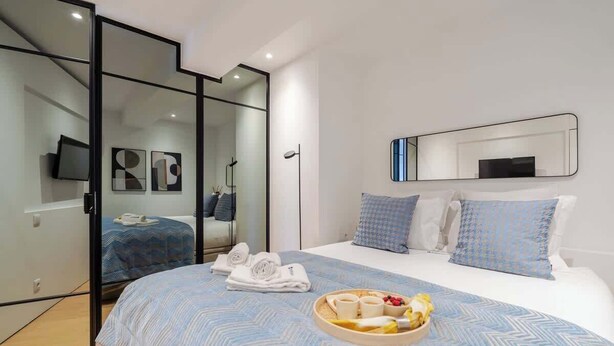 A modern hotel room with a large bed, a glass partition, and a breakfast tray on the bed. - Stylish Flat with Workspace & Garage by HostWise (Porto)