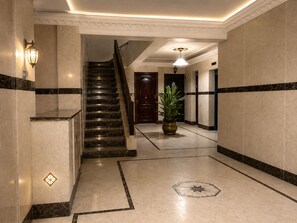 A hotel lobby with a marble staircase, a potted plant, and a geometric floor design.