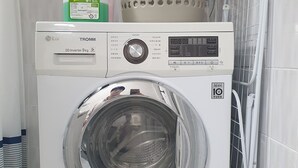 A front-loading washing machine with a control panel, detergent bottle, and a perforated laundry basket.