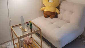A cozy room with a plush yellow teddy bear on a light-colored sofa, a small wooden side table with a mirror, a lamp, and a decorative tree.