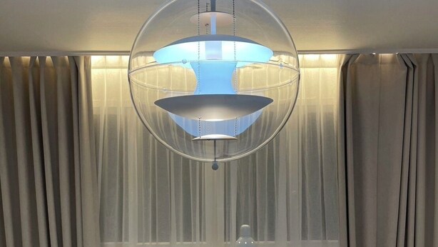 A hotel room with two beds, a hanging spherical light fixture, and sheer curtains.