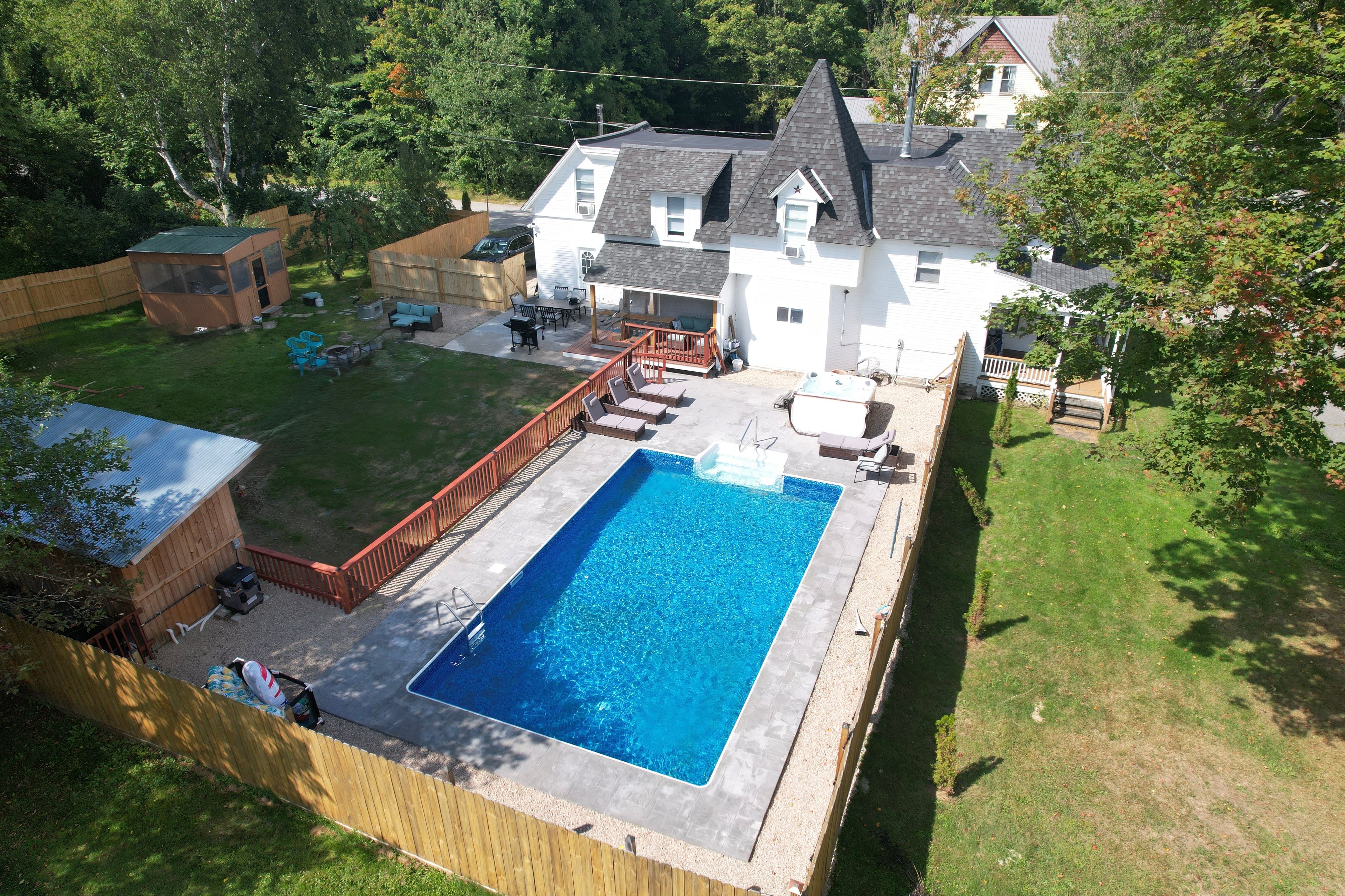 A residential backyard with a swimming pool, a wooden deck, and a fenced area.