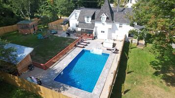 A residential backyard with a swimming pool, a wooden deck, and a fenced area.