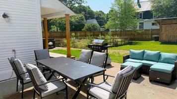 A patio with a table and chairs, a grill, and a sofa.
