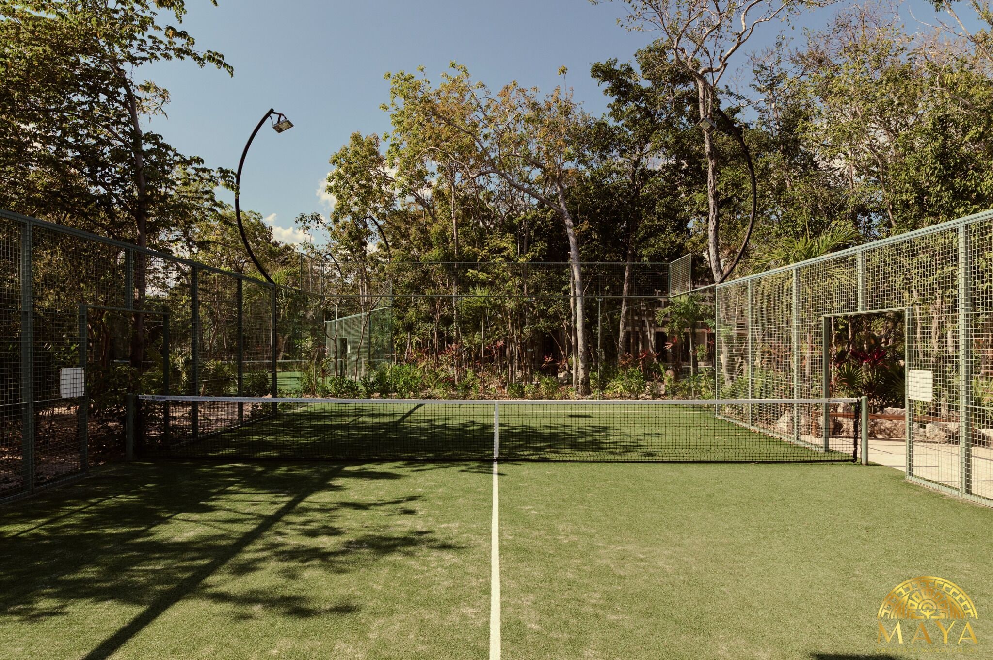 A tennis court with a net, surrounded by trees and a metal fence.