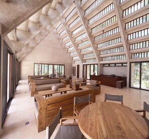 Un intérieur spacieux avec de hauts plafonds, de grandes fenêtres et un design moderne mettant en valeur des meubles en bois et une table ronde centrale.