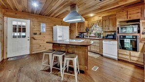 Eine Küchenzeile im Chalet-Stil mit einer Kochinsel, Barhocker, Kühlschrank, Mikrowelle, Backofen und Spüle.