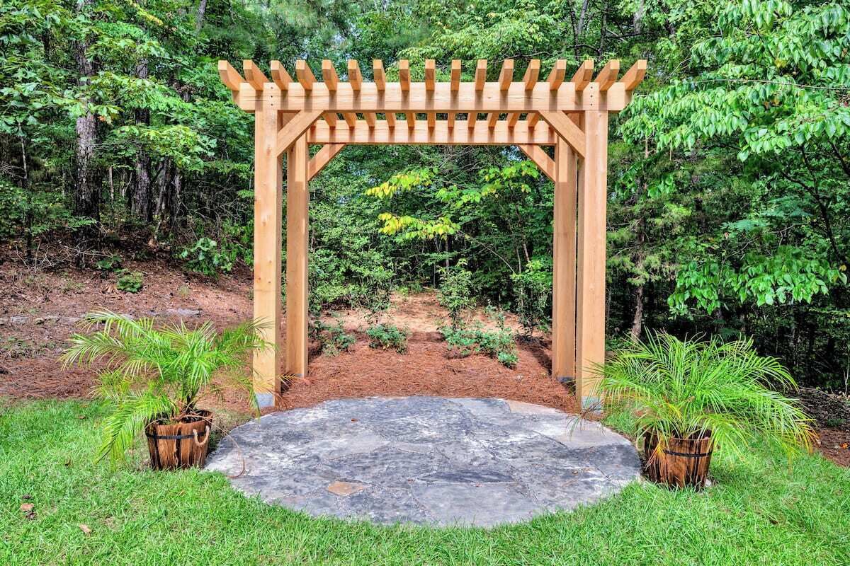 Una pérgola de madera con una plataforma circular de piedra en un jardín.