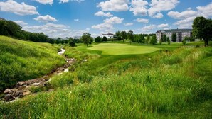 Un campo de golf con un arroyo, césped verde exuberante y un edificio al fondo.