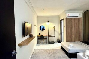 Habitación de hotel pequeña con cama, escritorio con silla, televisor y aire acondicionado.