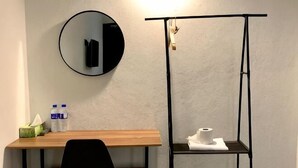 Una stanza con una scrivania, una sedia, uno specchio rotondo e un piccolo ripiano con articoli da toilette.