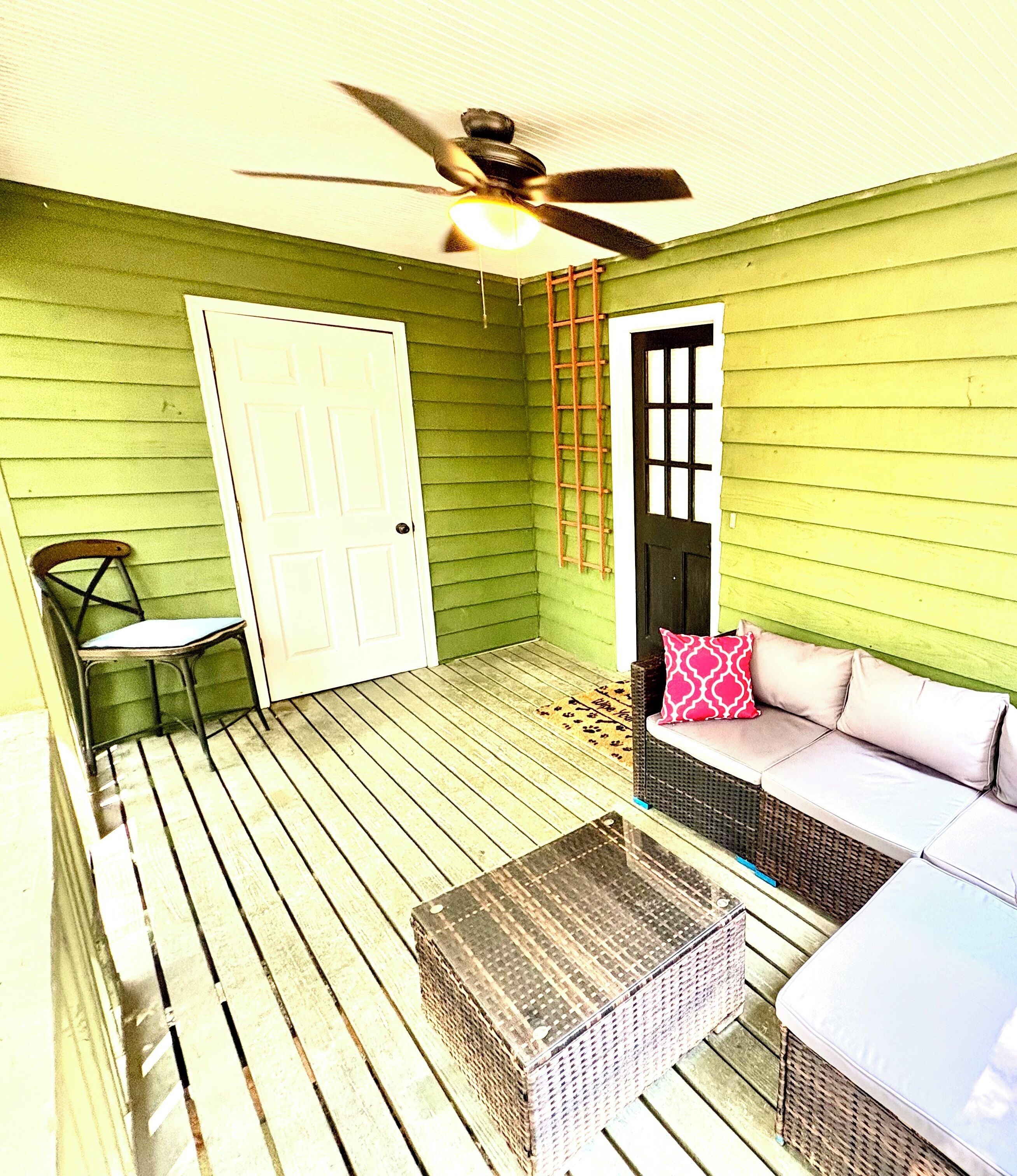 A green-walled room with a ceiling fan, a white door, a wicker bench, and a wicker table.
