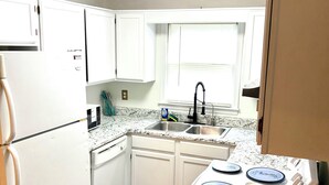 A kitchen with white cabinets, a stainless steel sink, a stove, and a refrigerator.
