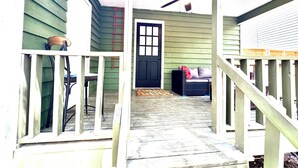 A porch with a black door, a ceiling fan, and a wicker sofa with cushions.