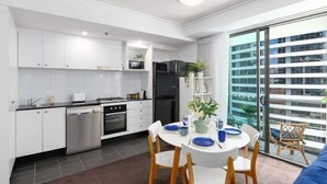 A modern kitchen with white cabinets, a dining table with blue plates, and a balcony with a view of a building.