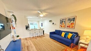 A modern living room with a blue sofa, a dining area with white chairs, and a kitchen in the background. - NEW Gorgeous Sunshine-Up 6 Guests-Private Backyard (Port Orange)