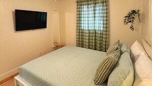 A bedroom with a bed, a ceiling fan, a TV mounted on the wall, and a window with curtains. - NEW Gorgeous Sunshine-Up 6 Guests-Private Backyard (Port Orange)