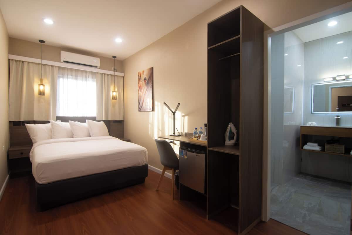 A hotel room with a bed, desk, chair, and a mirror.