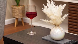A living room with a dark wooden coffee table, a vase with pampas grass, a glass of red wine, and a sign that says "TAKE VACATIONS". - Tstays Smart Hotel (Port of Spain)