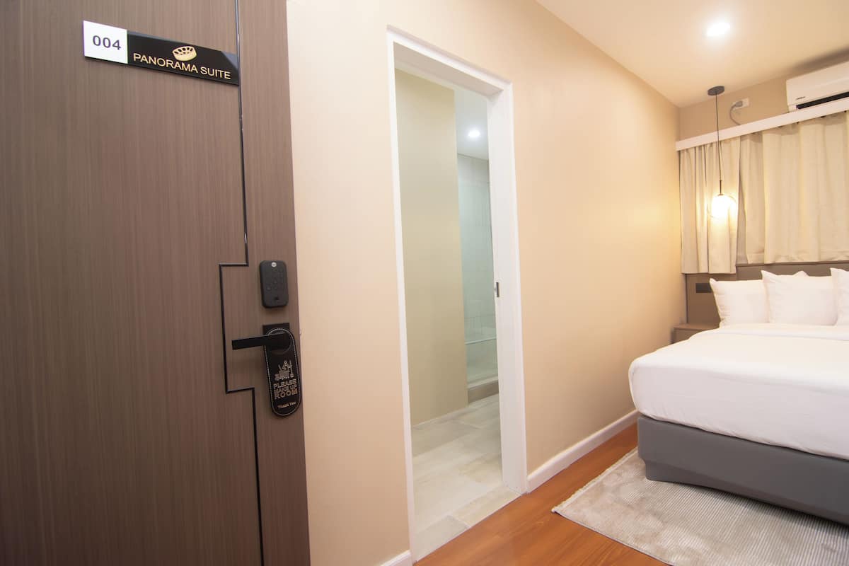 A hotel room with a bed, a door labeled '004 PANORAMA SUITE,' and a visible bathroom.