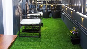A small outdoor area with artificial grass, a wooden bench, potted plants, and a railing. - Tstays Smart Hotel (Port of Spain)