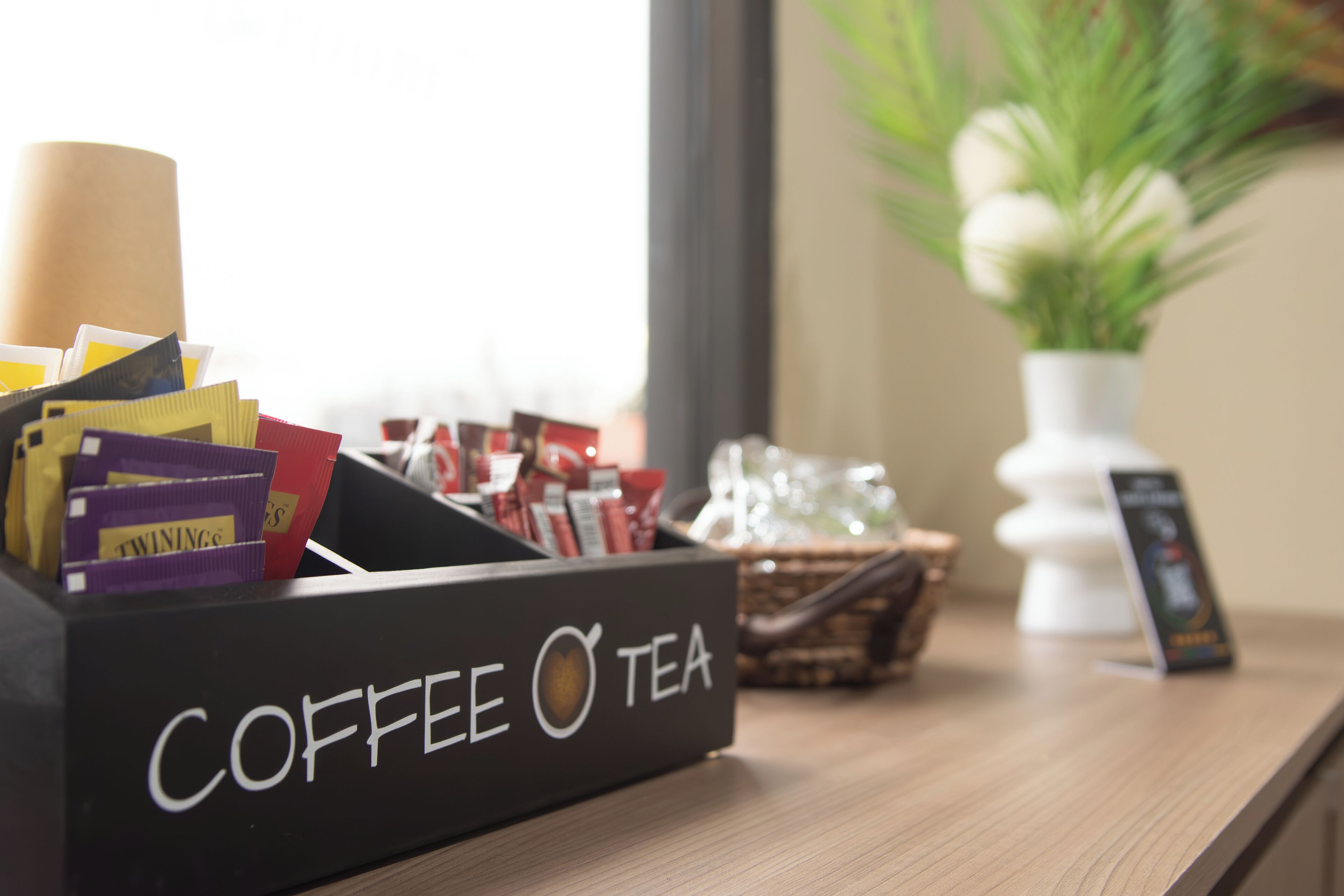 Un dispensador de café y té sobre una mesa de madera, con una ventana al fondo.