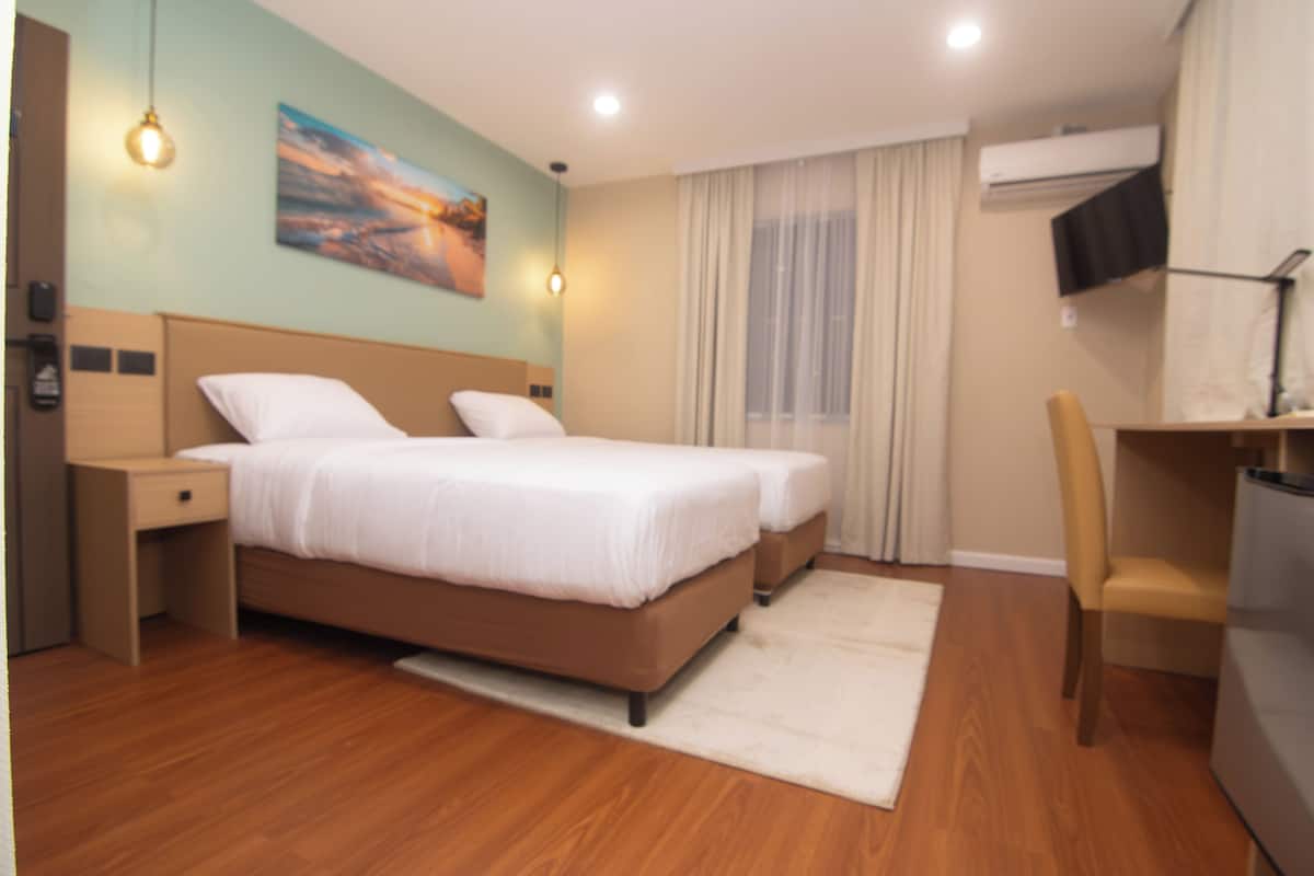 A modern hotel room with a large bed, a desk, a chair, and a TV.